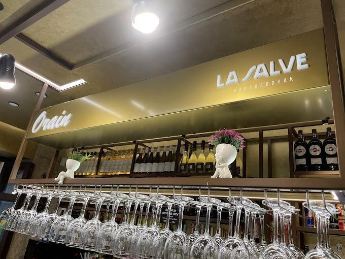 Un bar con copas de vino colgando del techo y un cartel que dice la salve