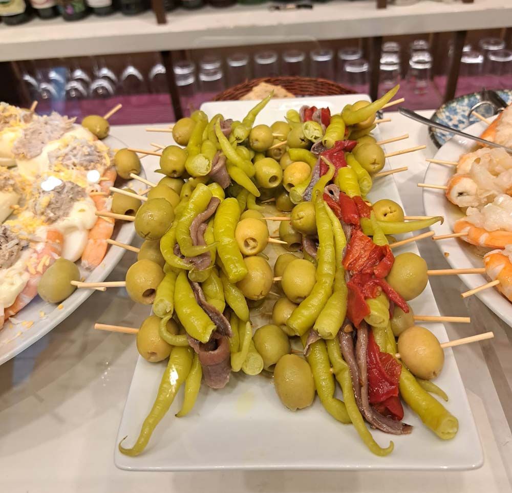 Un plato de comida con aceitunas y pimientos en brochetas sobre una mesa.