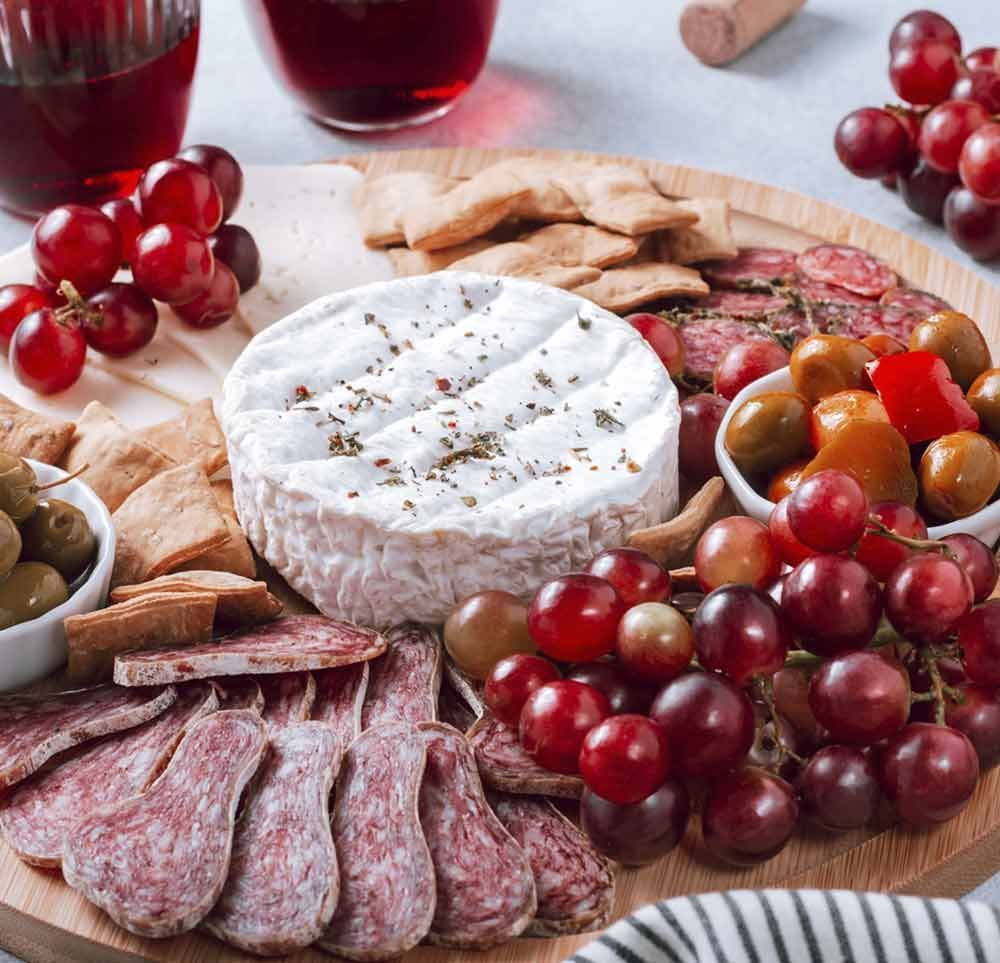 Una tabla de cortar de madera llena de una variedad de alimentos, incluidas uvas y queso.