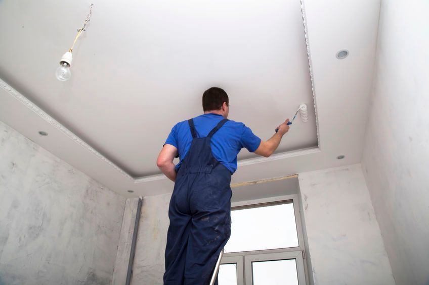 Un hombre está pintando el techo de una habitación con un rodillo.