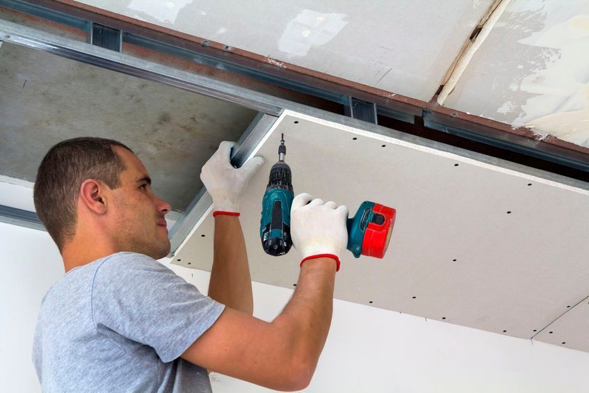Un hombre está usando un taladro para instalar un techo de yeso.