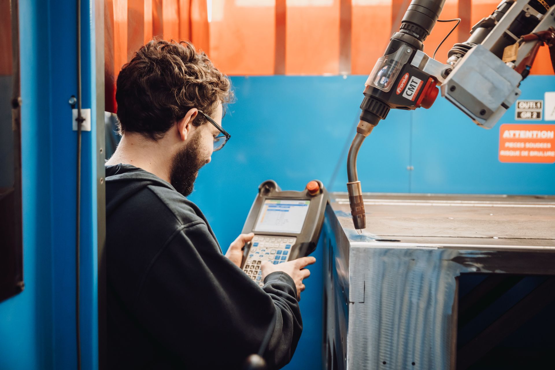 Un homme manipule un bras de soudage robotisé et regarde le panneau de commande dans l'atelier