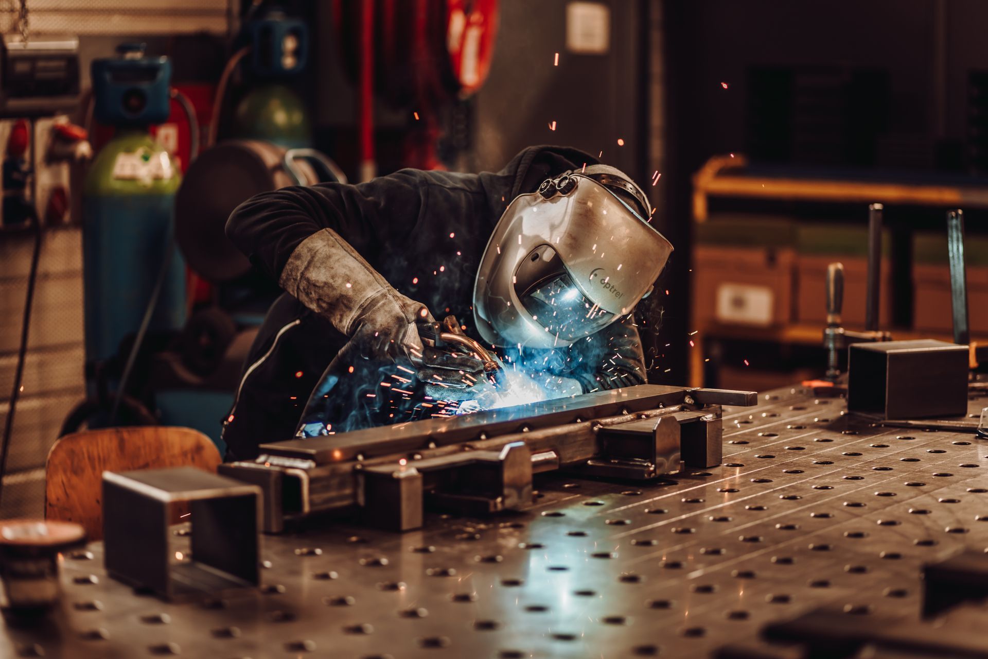 Un soudeur dans un atelier, portant un casque et des gants, soude du métal, des étincelles volent