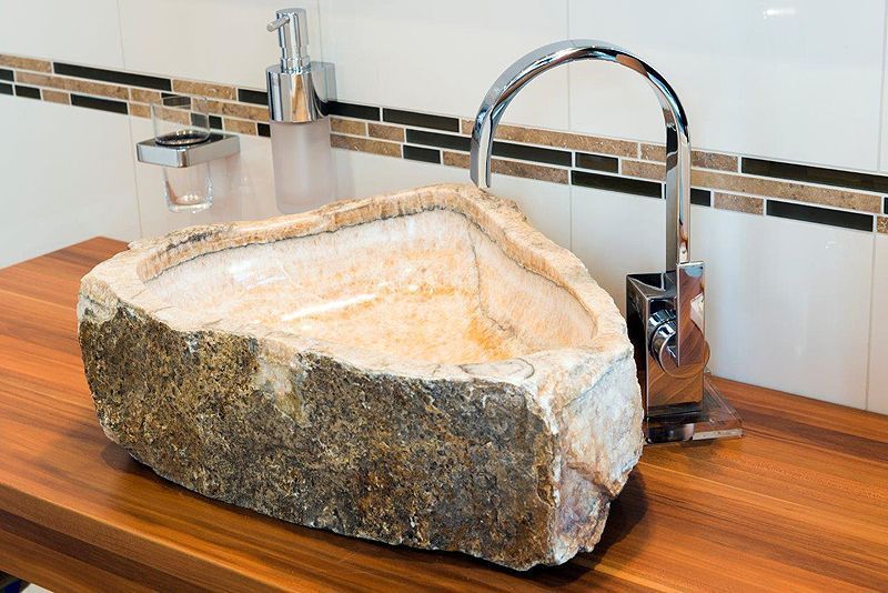 Ein Waschbecken mit Wasserhahn und Seifenspender auf einer Holzablage.