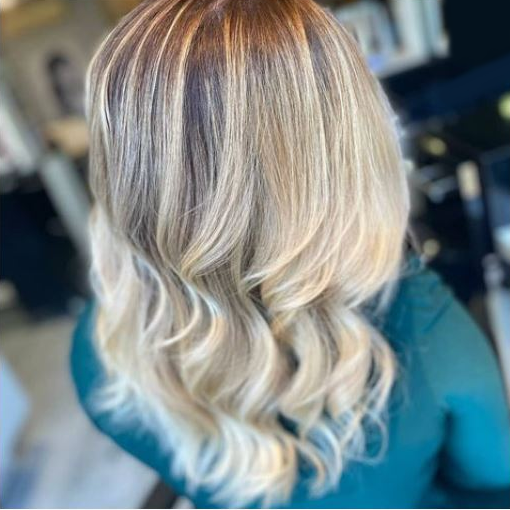 Personne avec des cheveux longs et ondulés, colorés en blond, dans un salon de coiffure