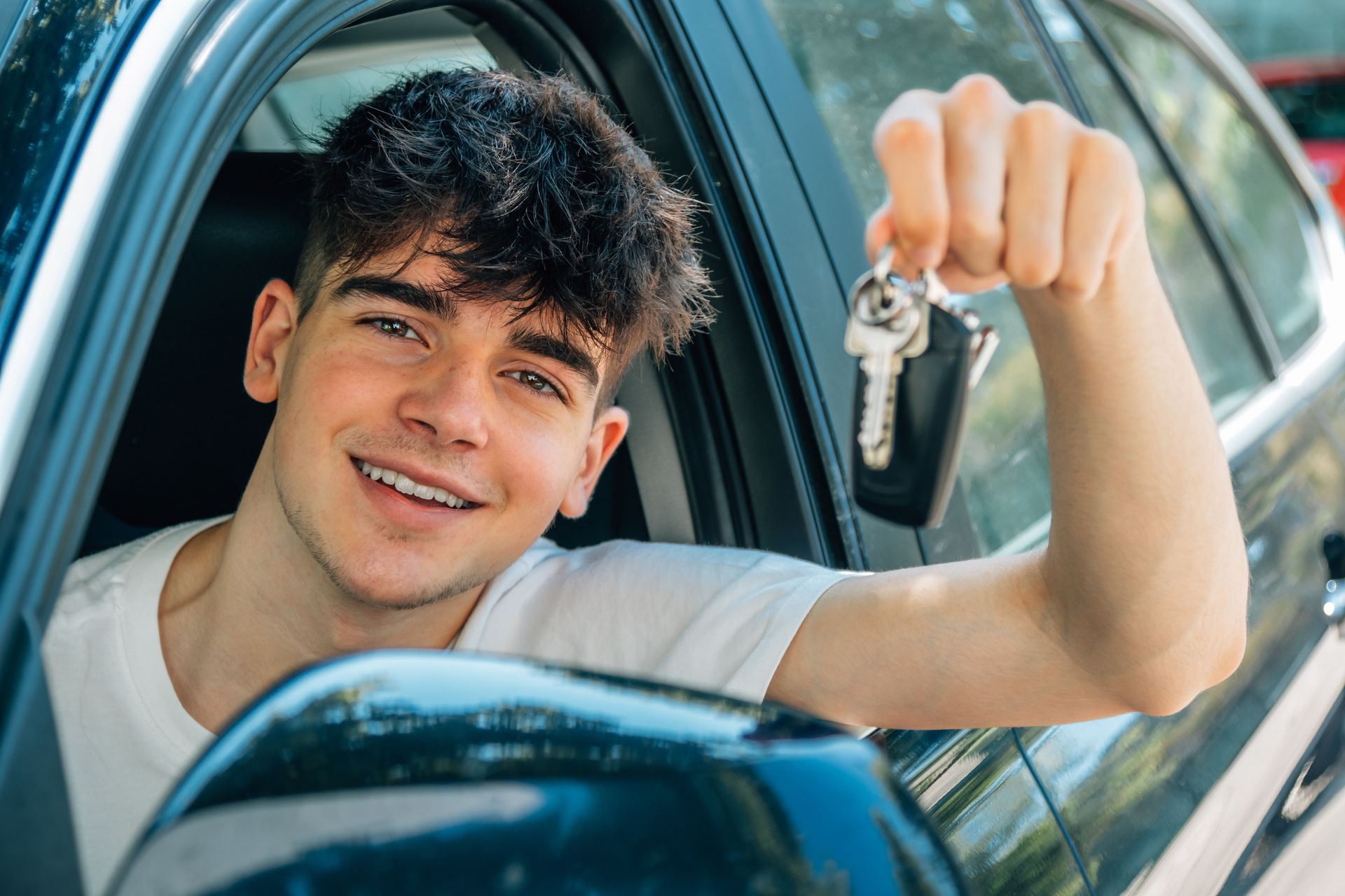 Jeune personne en voiture, souriante, brandissant ses clés de voiture.