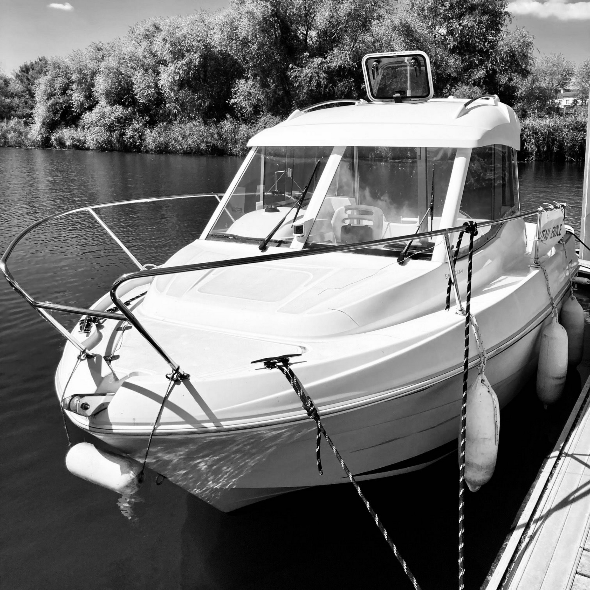 Un bateau navigue sur un canal par une journée ensoleillée. Eau verte, ciel bleu, arbres en arrière-plan.