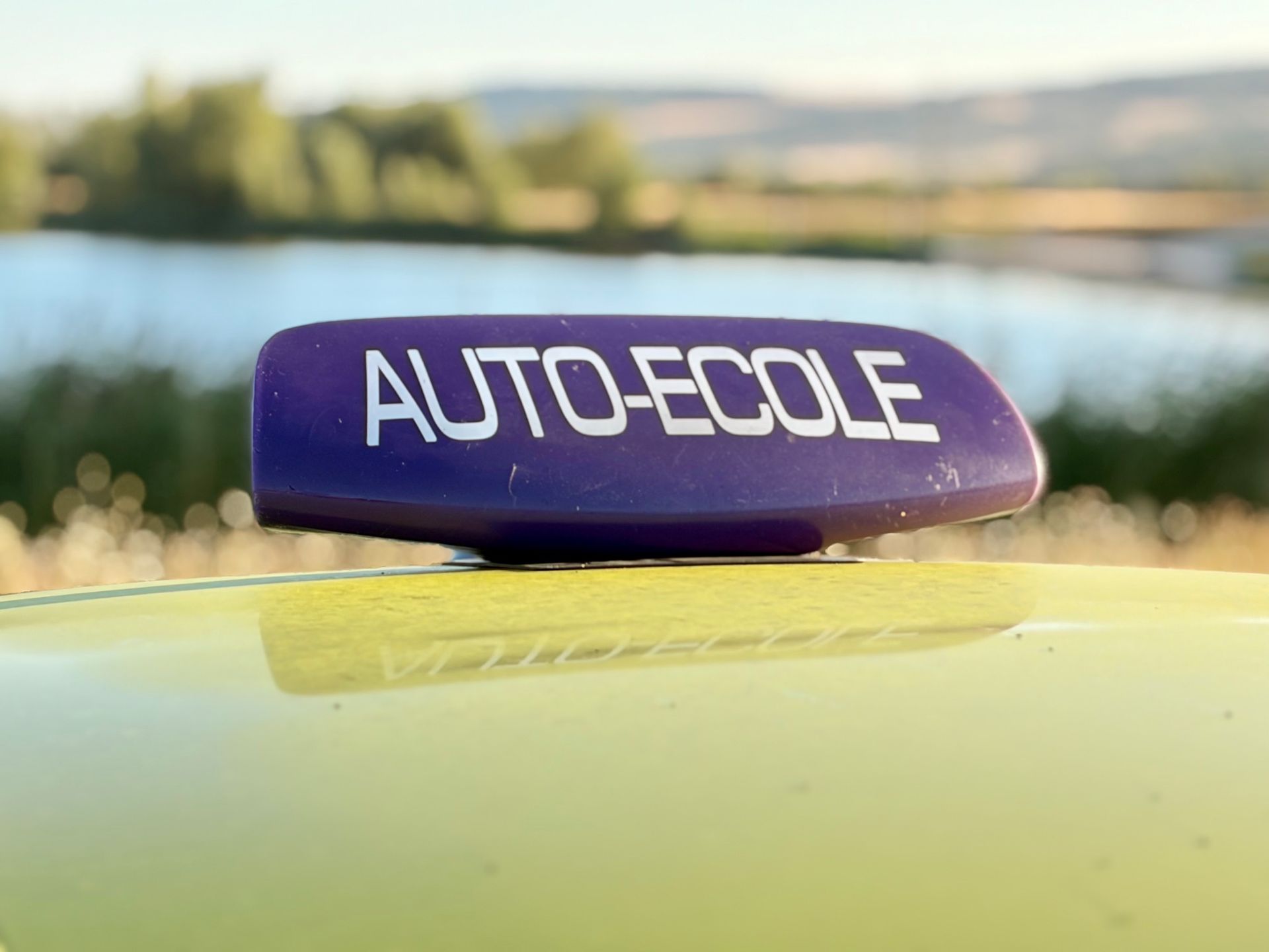 Panneau blanc AUTO-ÉCOLE sur une voiture rouge, avec une antenne noire.