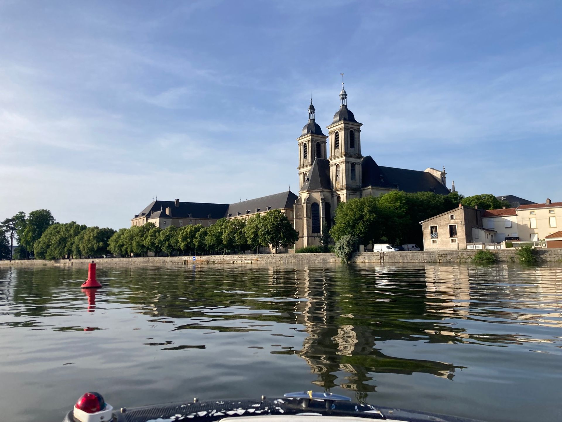 Église aux deux clochers se reflétant dans l'eau, bouée rouge au premier plan, sous un ciel bleu.