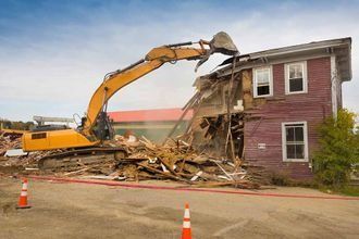 Una excavadora amarilla está demoliendo una casa de ladrillos.