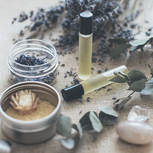 Ätherische Ölprodukte mit Lavendelknospen, Eukalyptus und einem dekorativen Stein auf neutralem Untergrund.