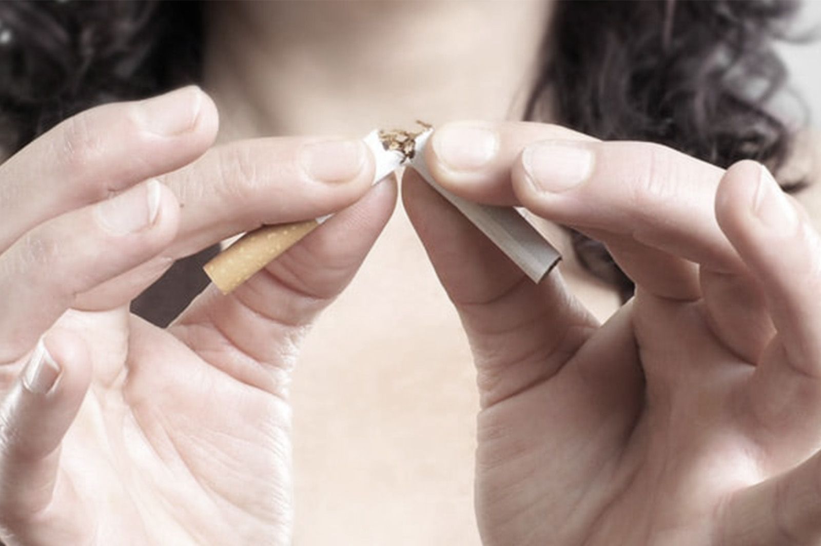 Hände brechen eine Zigarette in zwei Hälften.