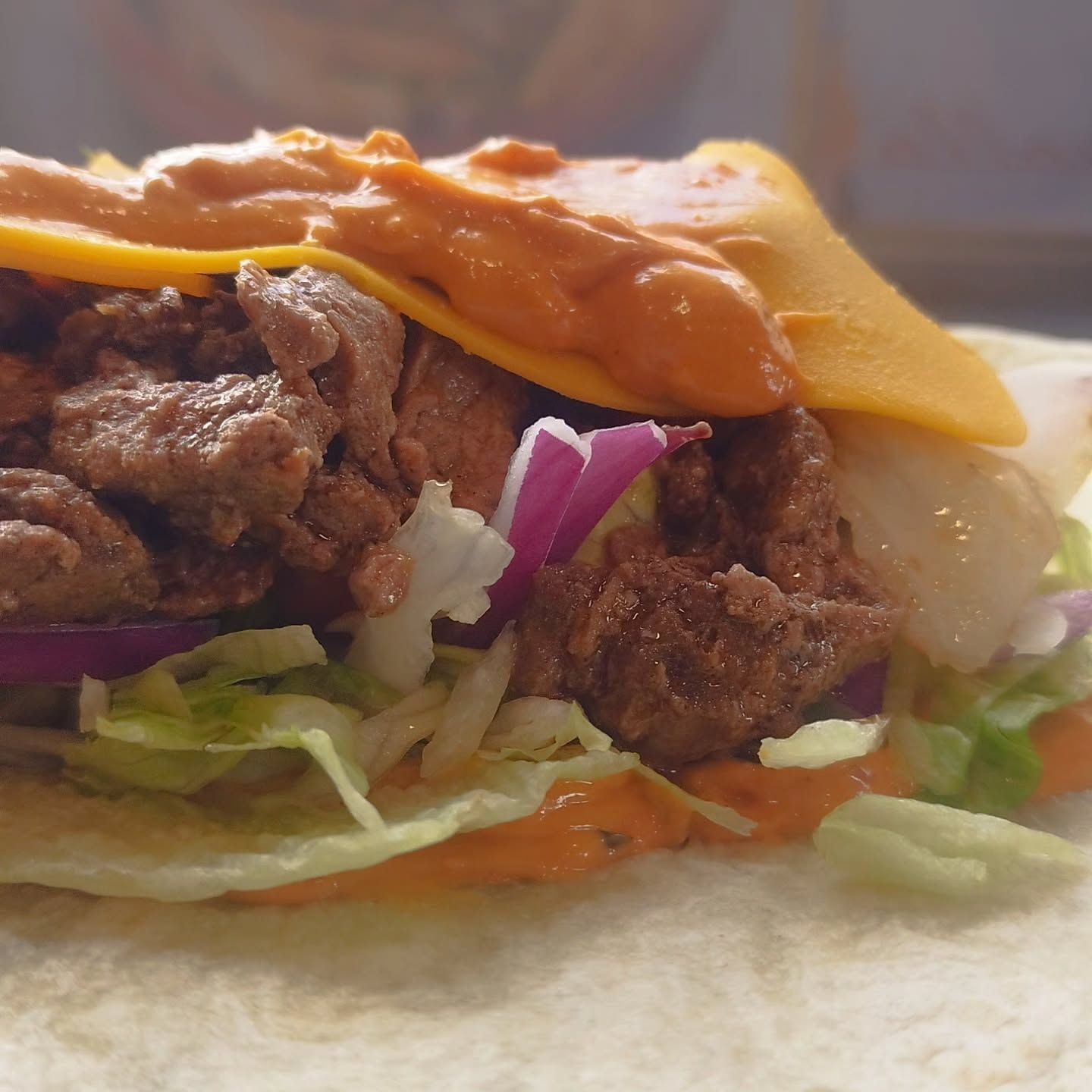 Un primer plano de un taco con carne, queso, lechuga y cebolla.