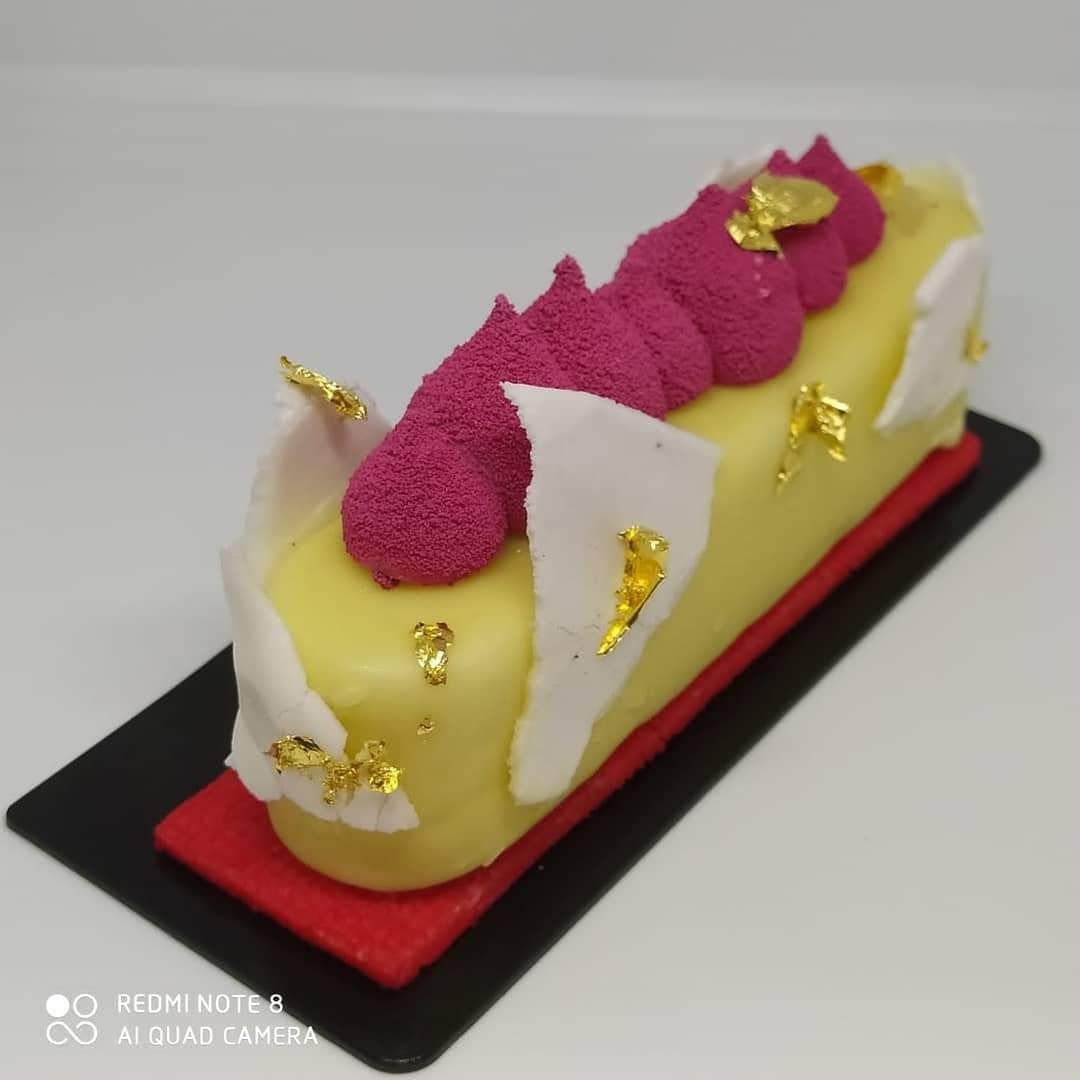 Un pastel amarillo con glaseado rosa y pan de oro en la parte superior.