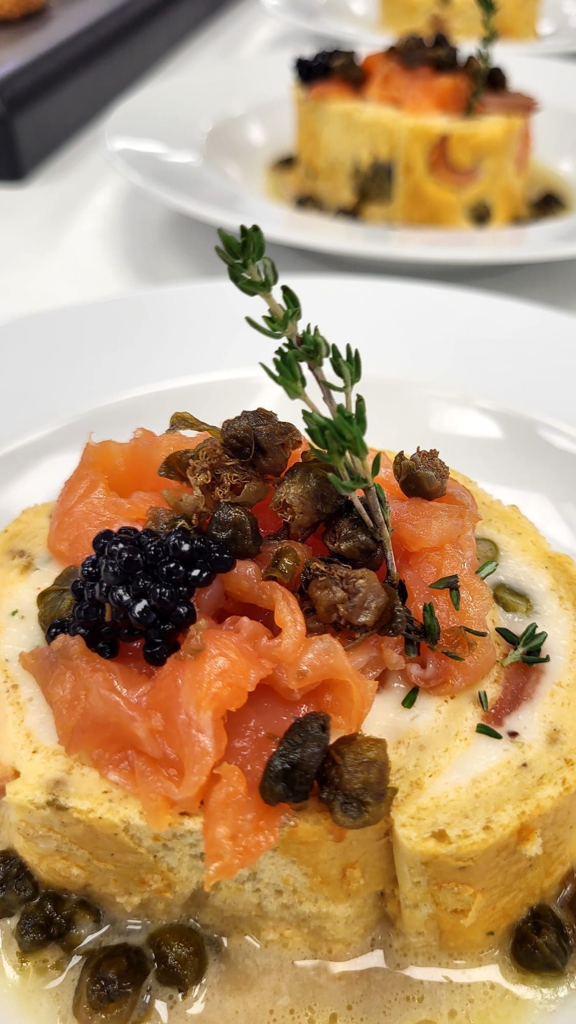 Aperitivo de salmón con caviar, alcaparras, ramita de tomillo, en plato blanco.