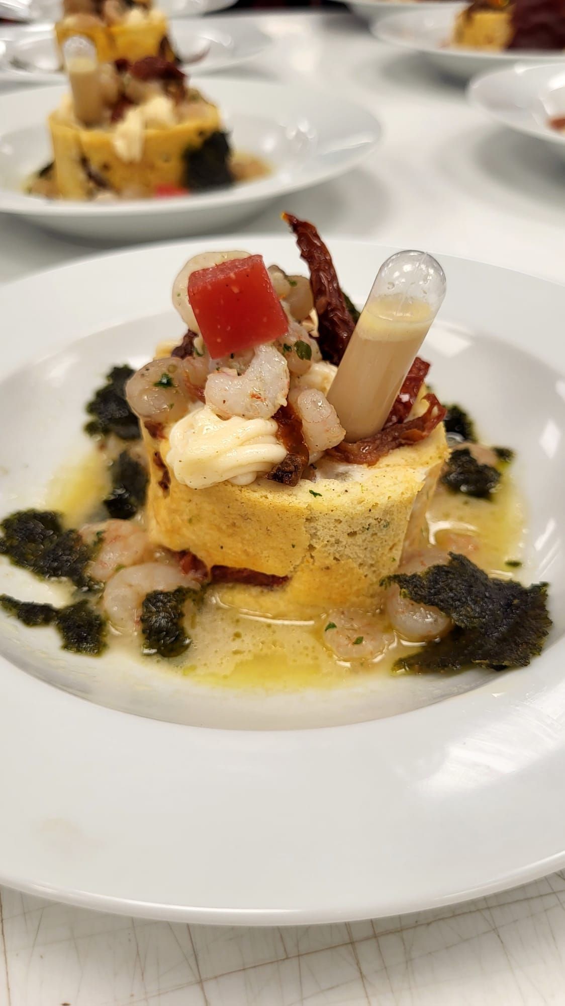 Pastel de polenta amarilla con camarones, tomate, salsa y algas en un plato blanco.