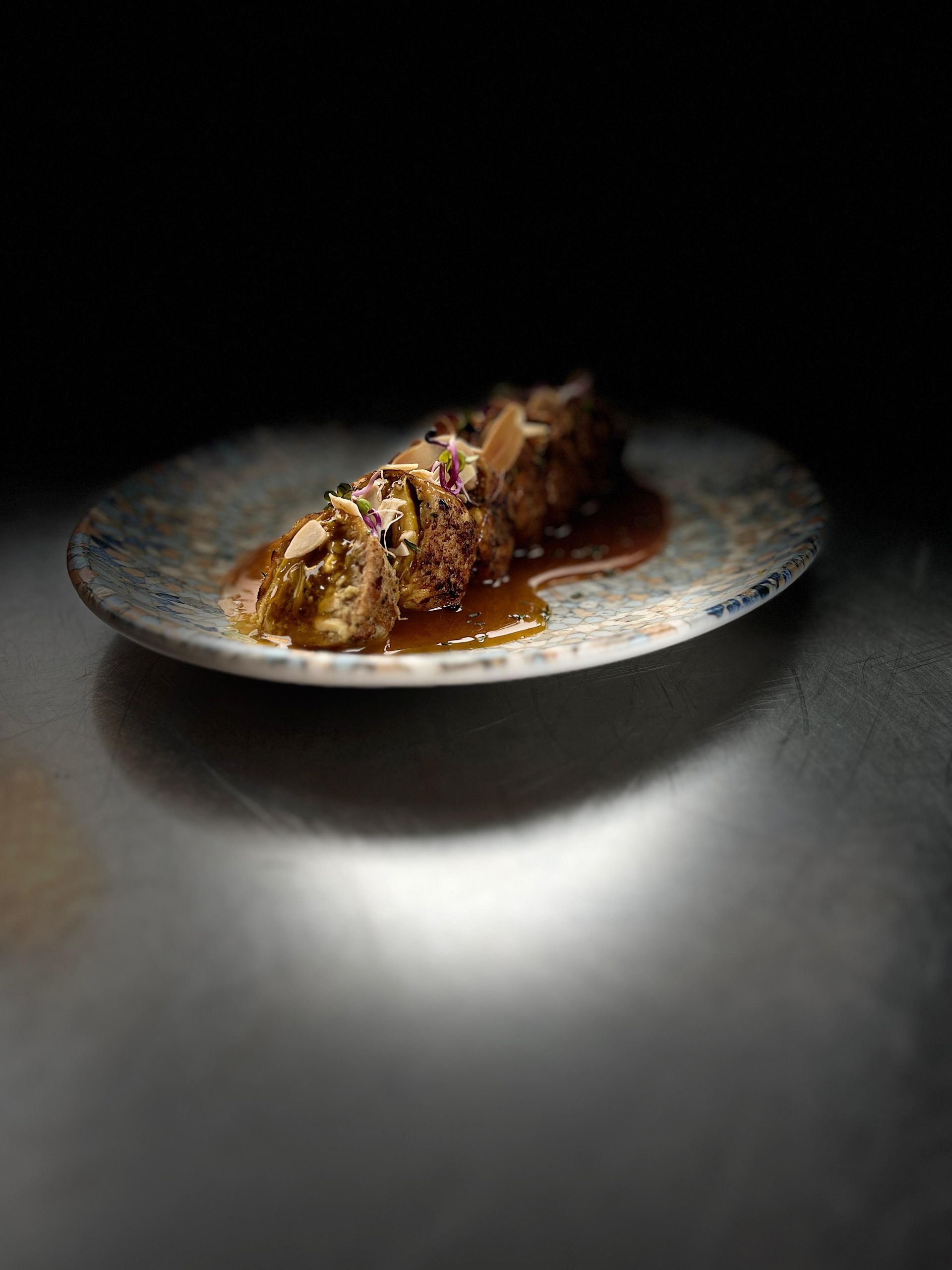 Plato de comida en un plato moteado, con salsa. Fondo oscuro.