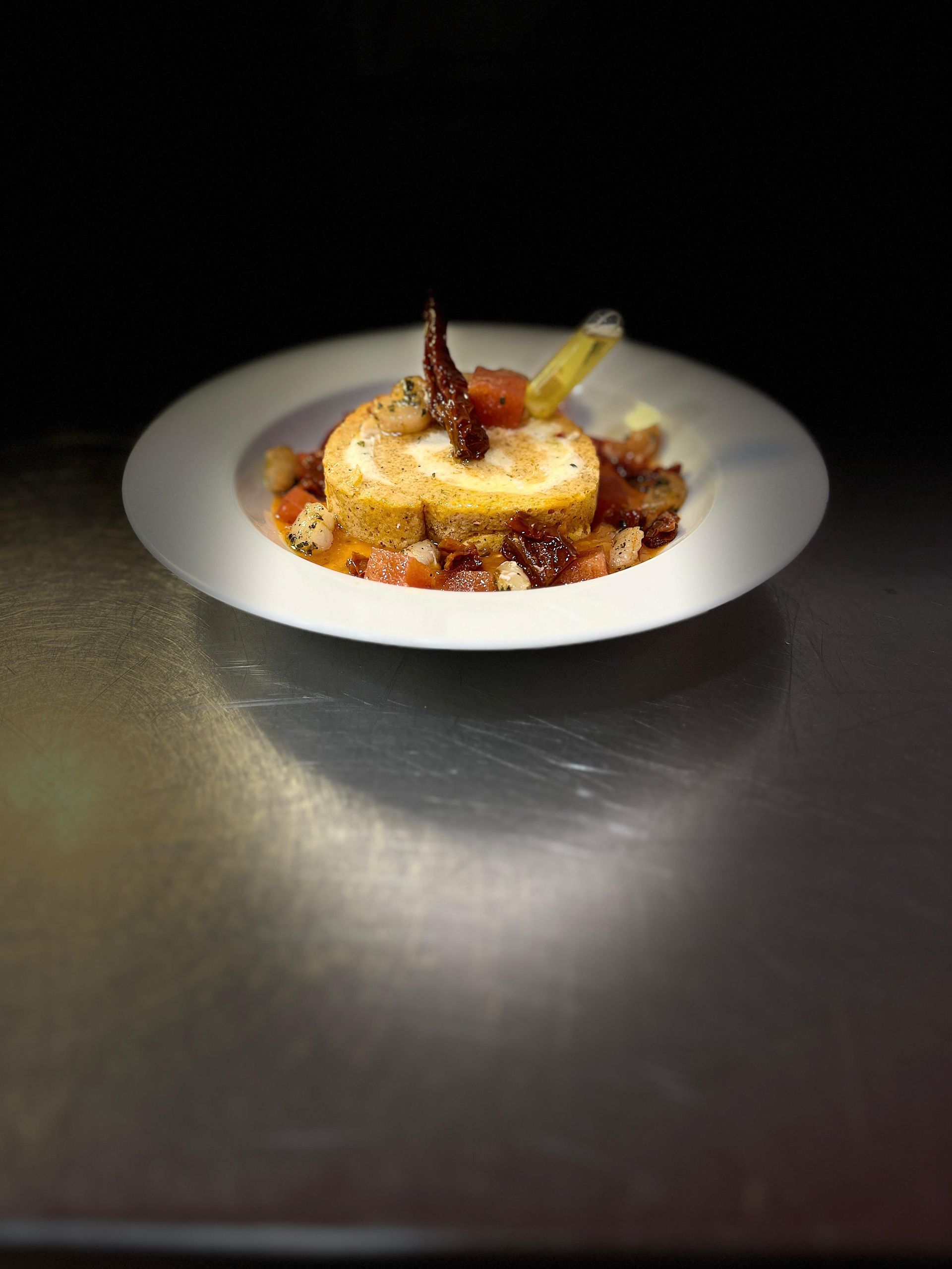 Un alimento redondo, de color marrón dorado, sobre un plato blanco, con un acabado oscuro y una superficie de metal.