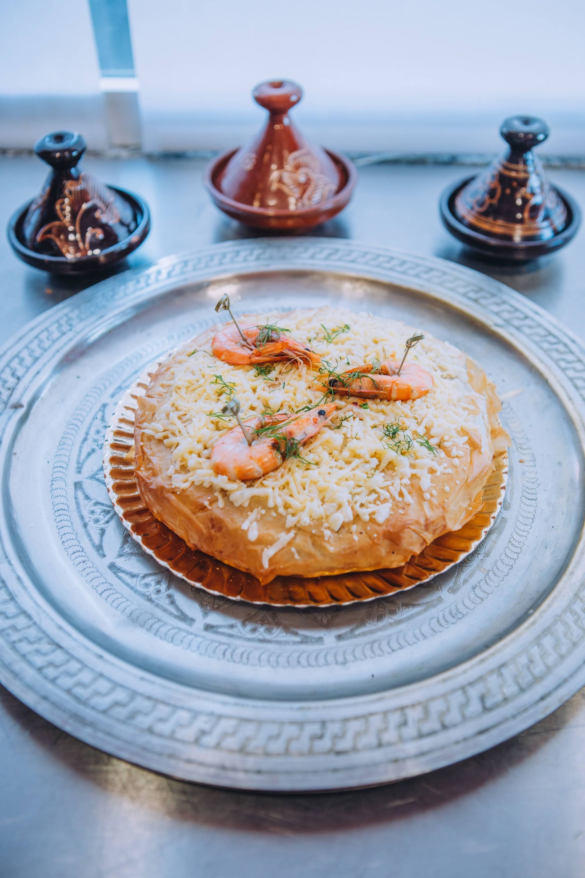 Una pizza con camarones y queso está en un plato de plata.