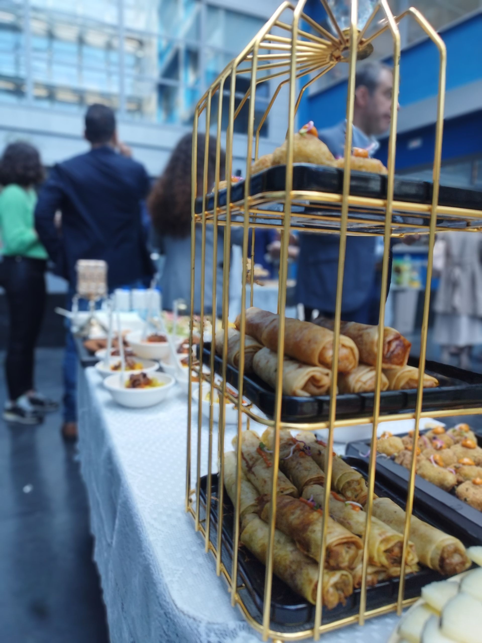Buffet con expositor dorado de varios rollos salados; gente en el fondo.