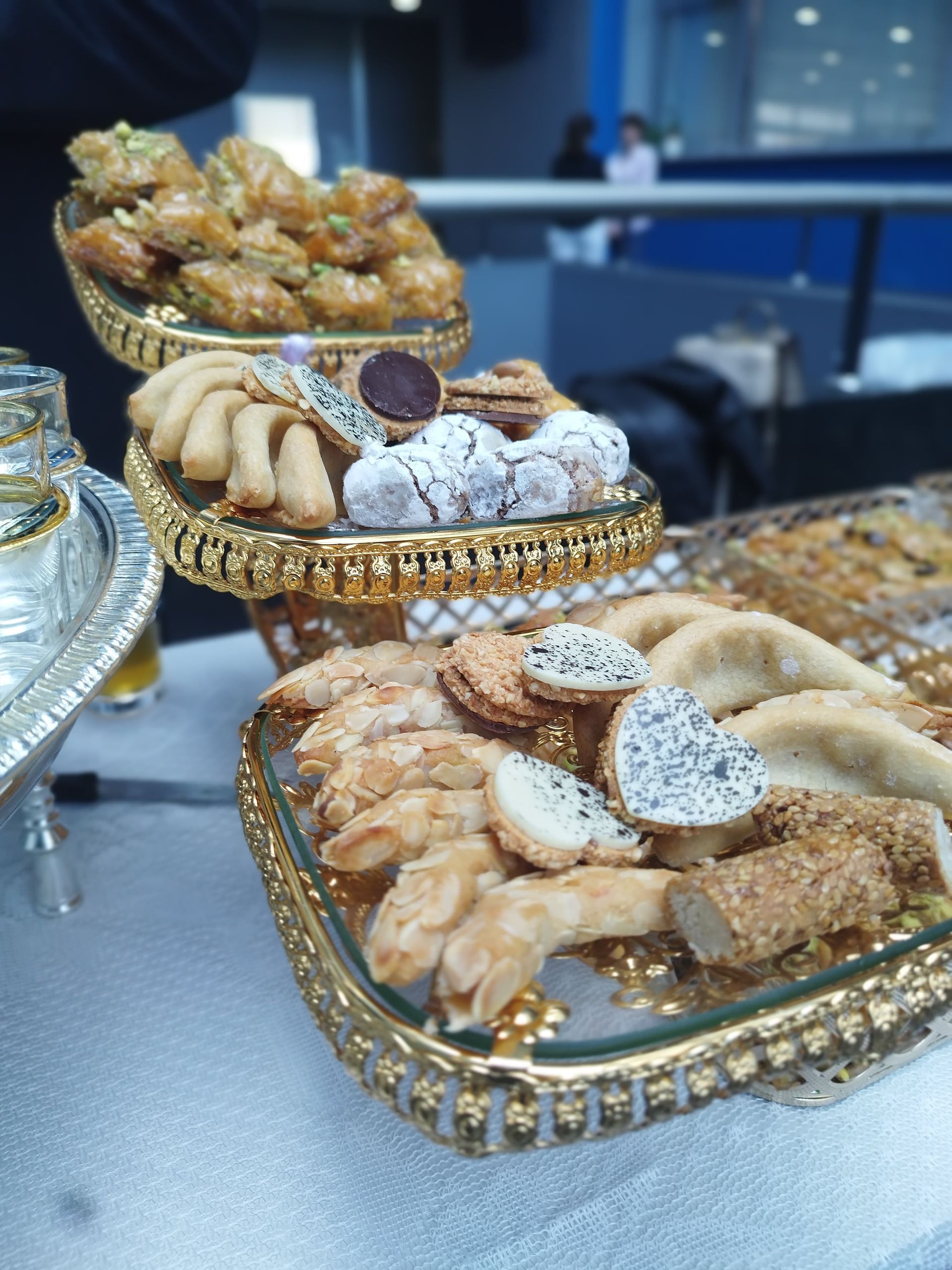 Exhibición de tres niveles de bandejas doradas y ornamentadas que contienen una variedad de pasteles horneados; una disposición de mesa.