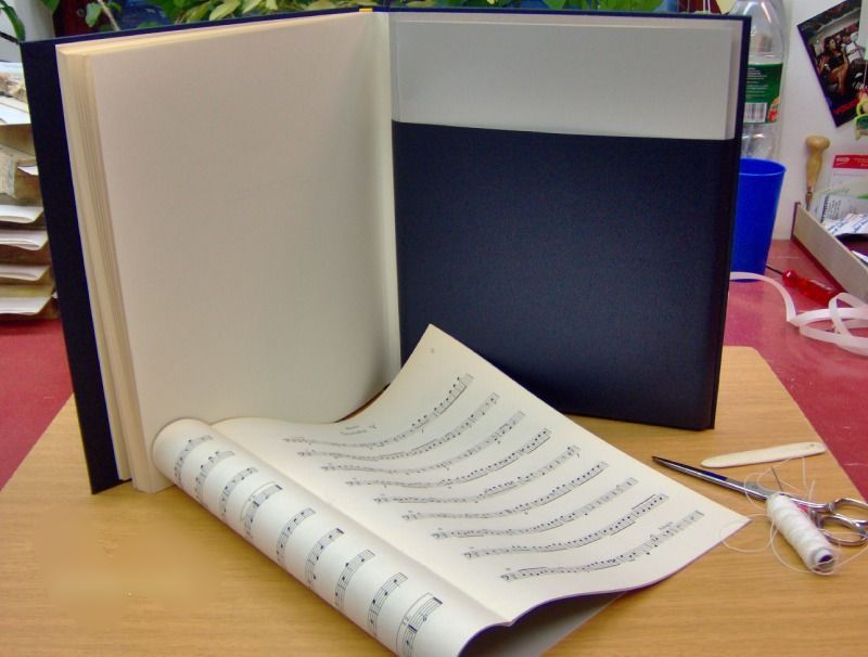 Schmales Musikbuch, das vor einem blau eingebundenen Buch mit leeren Seiten liegt.