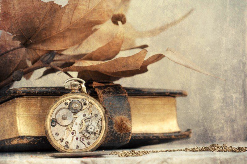 Antikes Buch mit Einband, vor dem eine antike Uhr liegt.