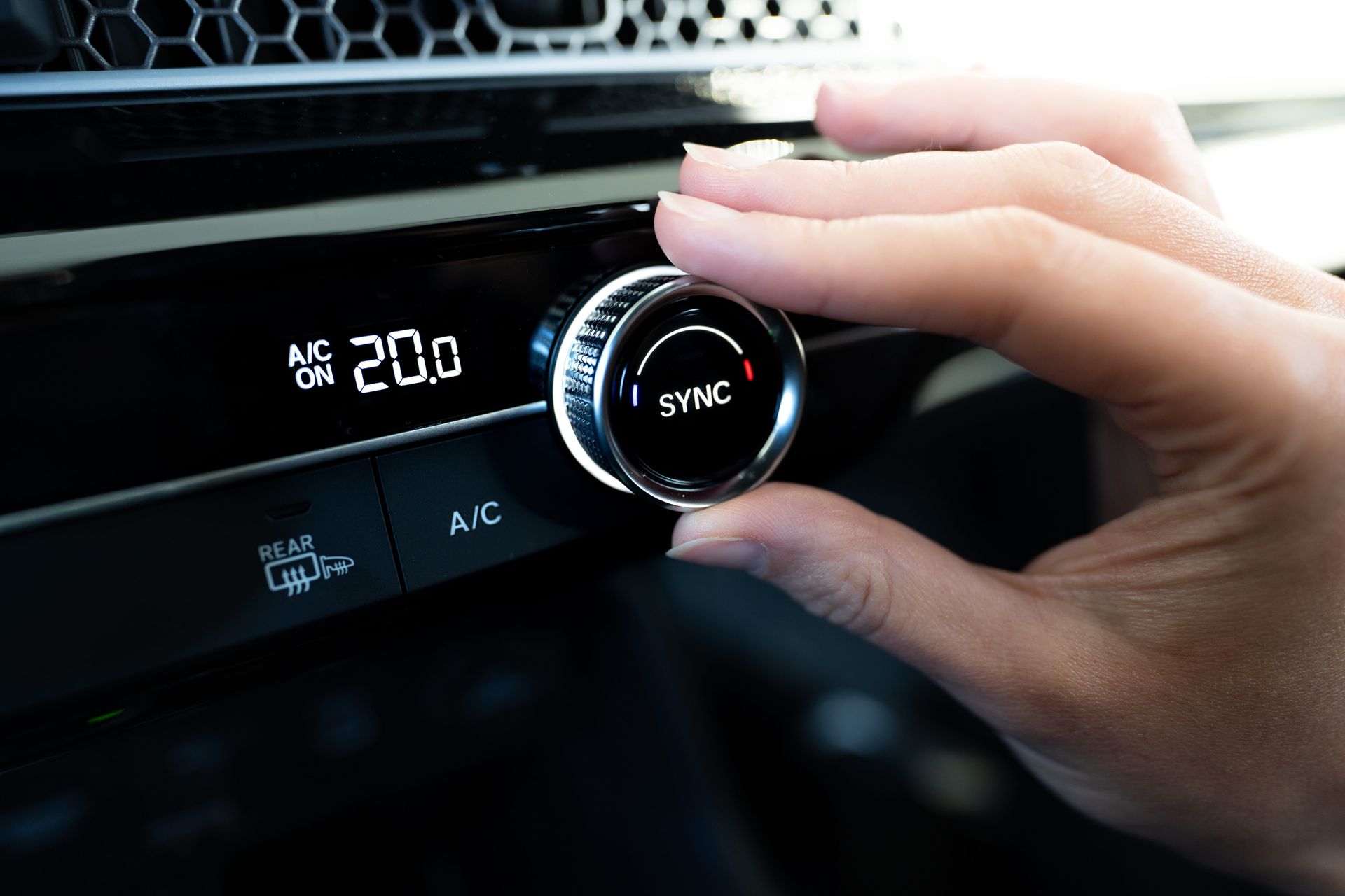 Main ajustant le bouton d’un autoradio, dont l’écran bleu affiche 20° et SYNC