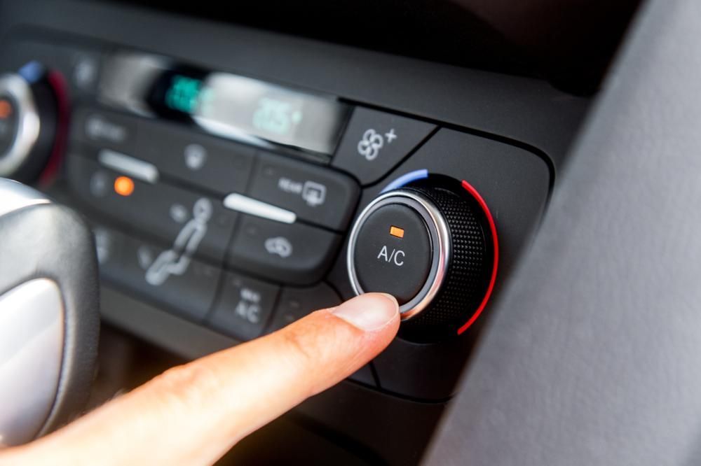 Doigt appuyant sur le bouton de climatisation d’un panneau de commande de climatisation automobile, avec un anneau rouge lumineux