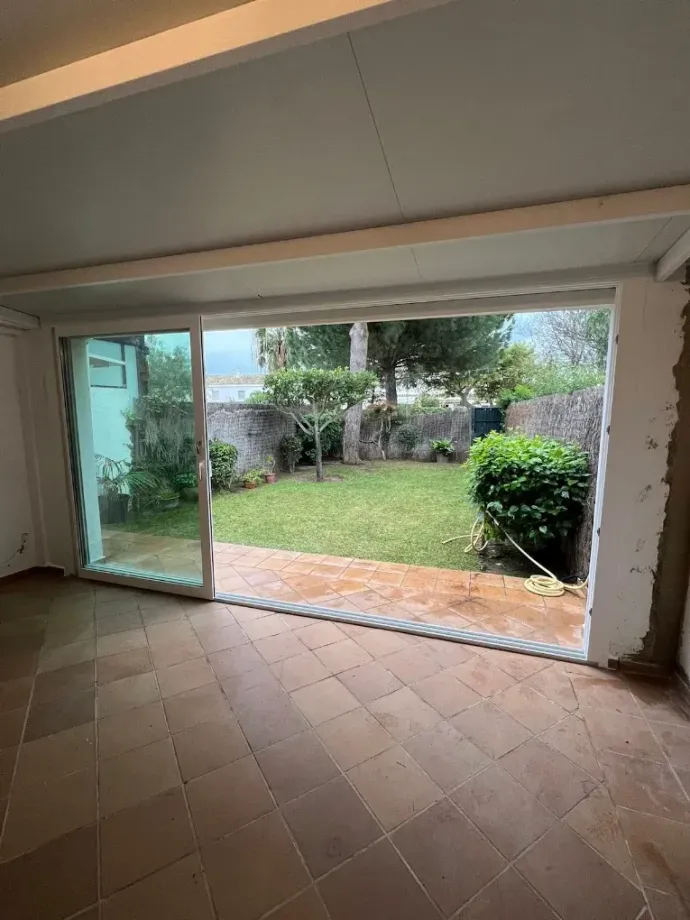 Habitación interior con suelo de baldosas que se abre a un pequeño patio y jardín trasero a través de puertas.