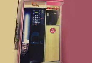 Máquina expendedora, negra y rosa, con un panel de botones, un vaso y aperitivos.