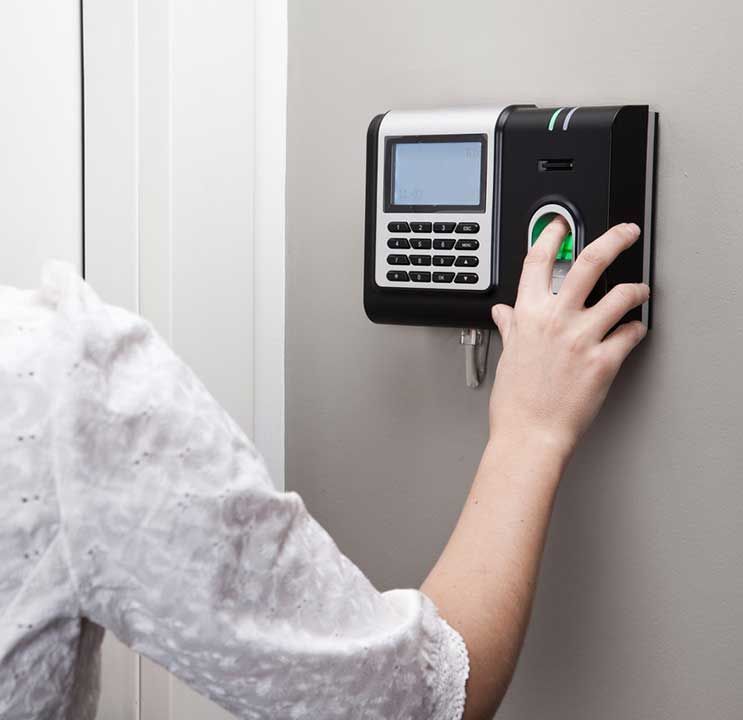 Une main scanne son empreinte digitale sur une pointeuse noire et argentée fixée sur un mur gris.