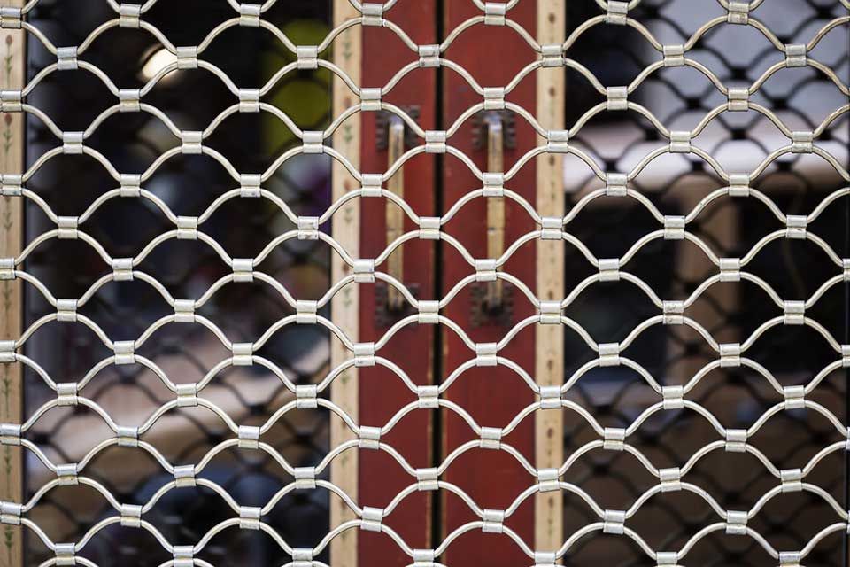Grille de sécurité au-dessus d'une porte rouge. Motif en grille métallique blanche.