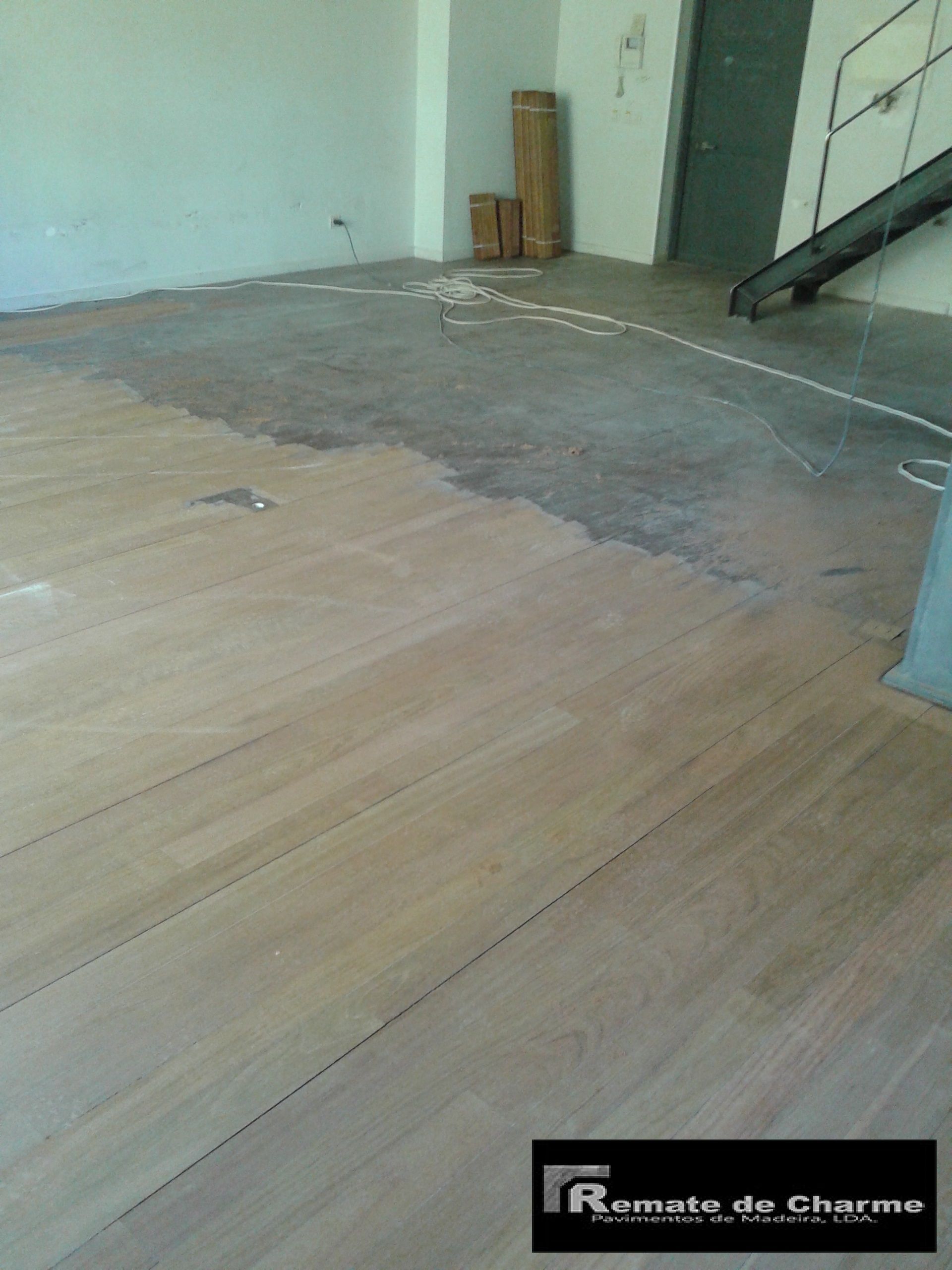 Piso de madeira parcialmente instalado em uma sala, com concreto e uma escada ao fundo.
