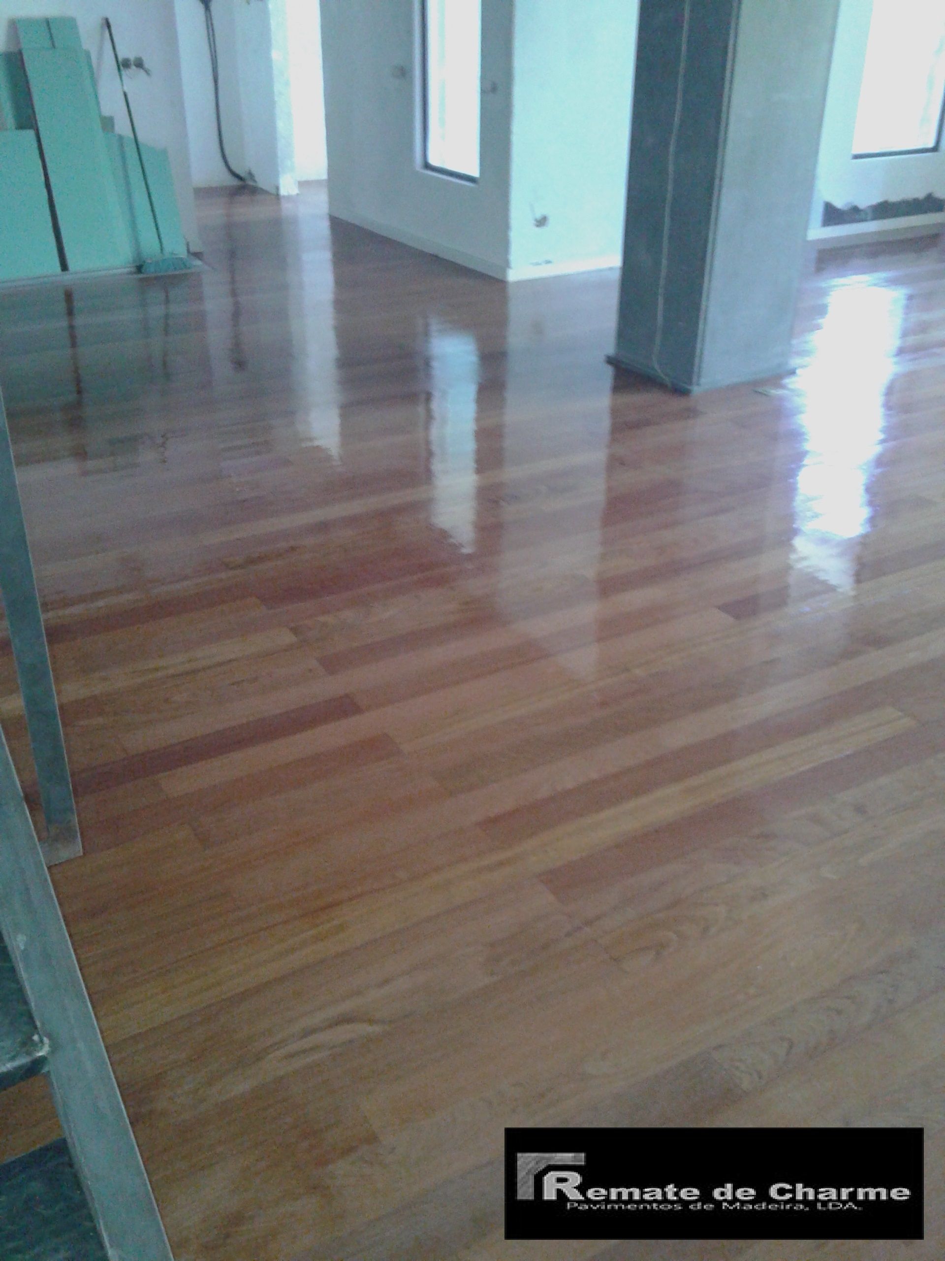 Piso de madeira brilhante e recém-acabado em uma sala aberta, refletindo a luz.