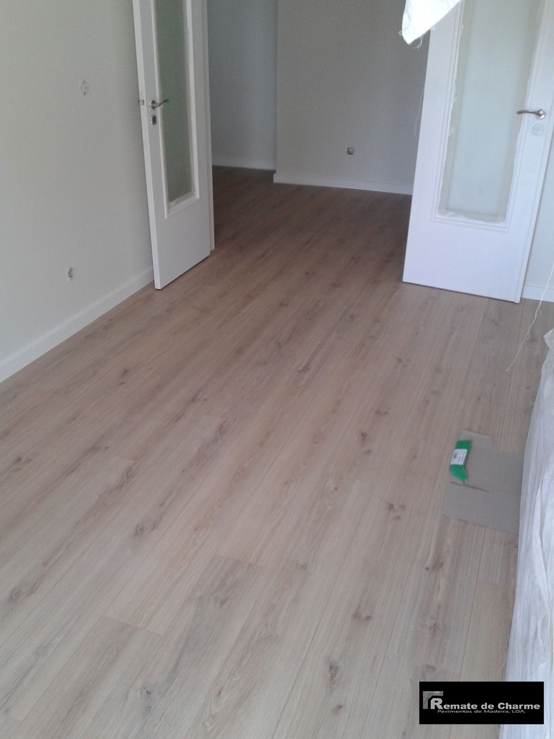 Piso com aparência de madeira clara em uma sala com paredes brancas e duas portas.