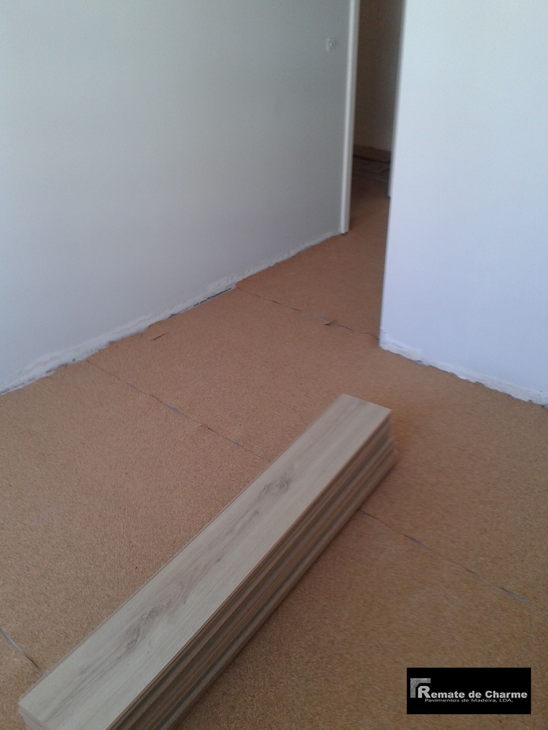 Tábuas de madeira sobre um forro de cortiça em uma sala com paredes brancas, aguardando instalação.