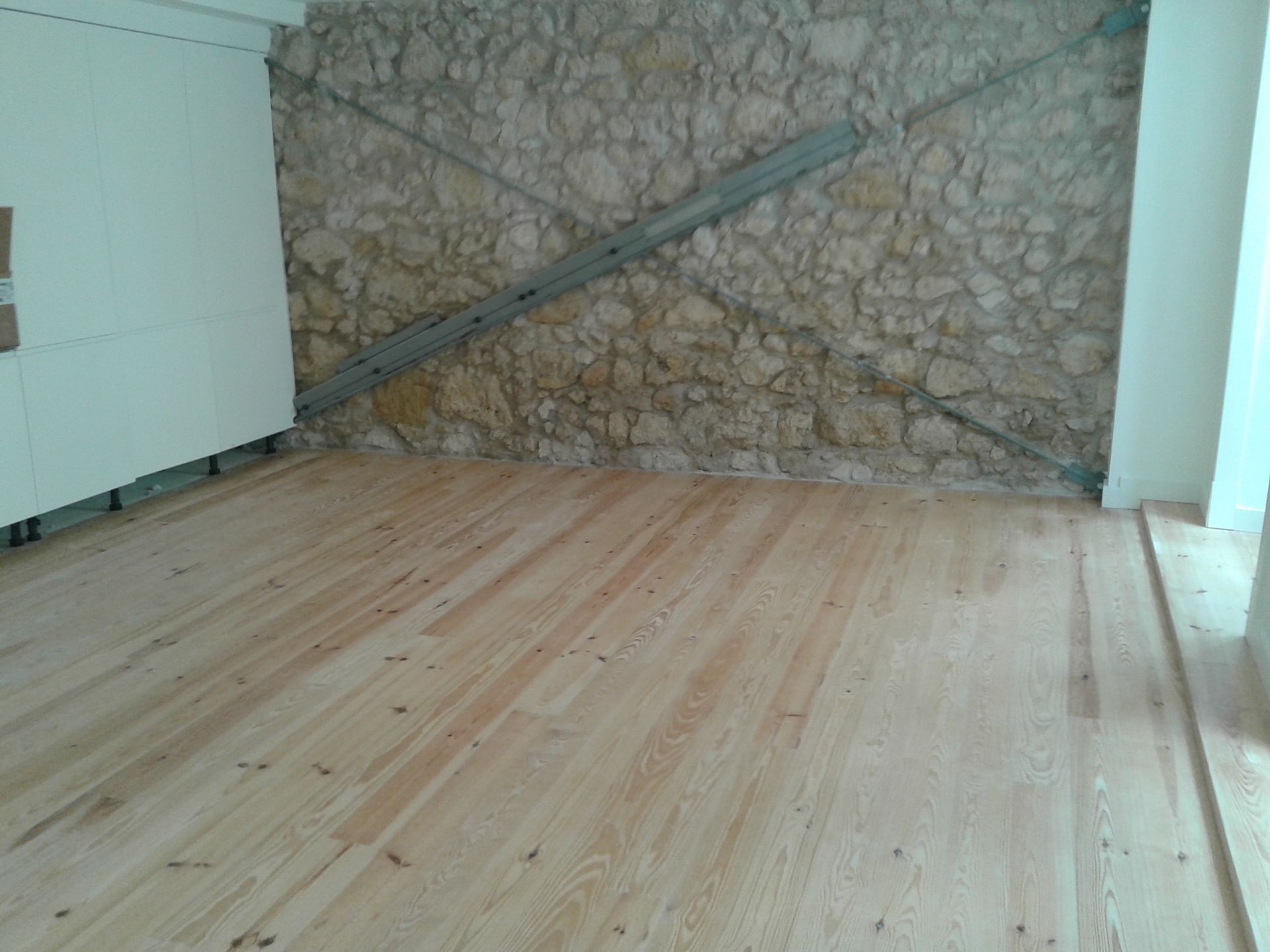 Piso de madeira em uma sala com parede de pedra; vigas de metal sustentam a parede.