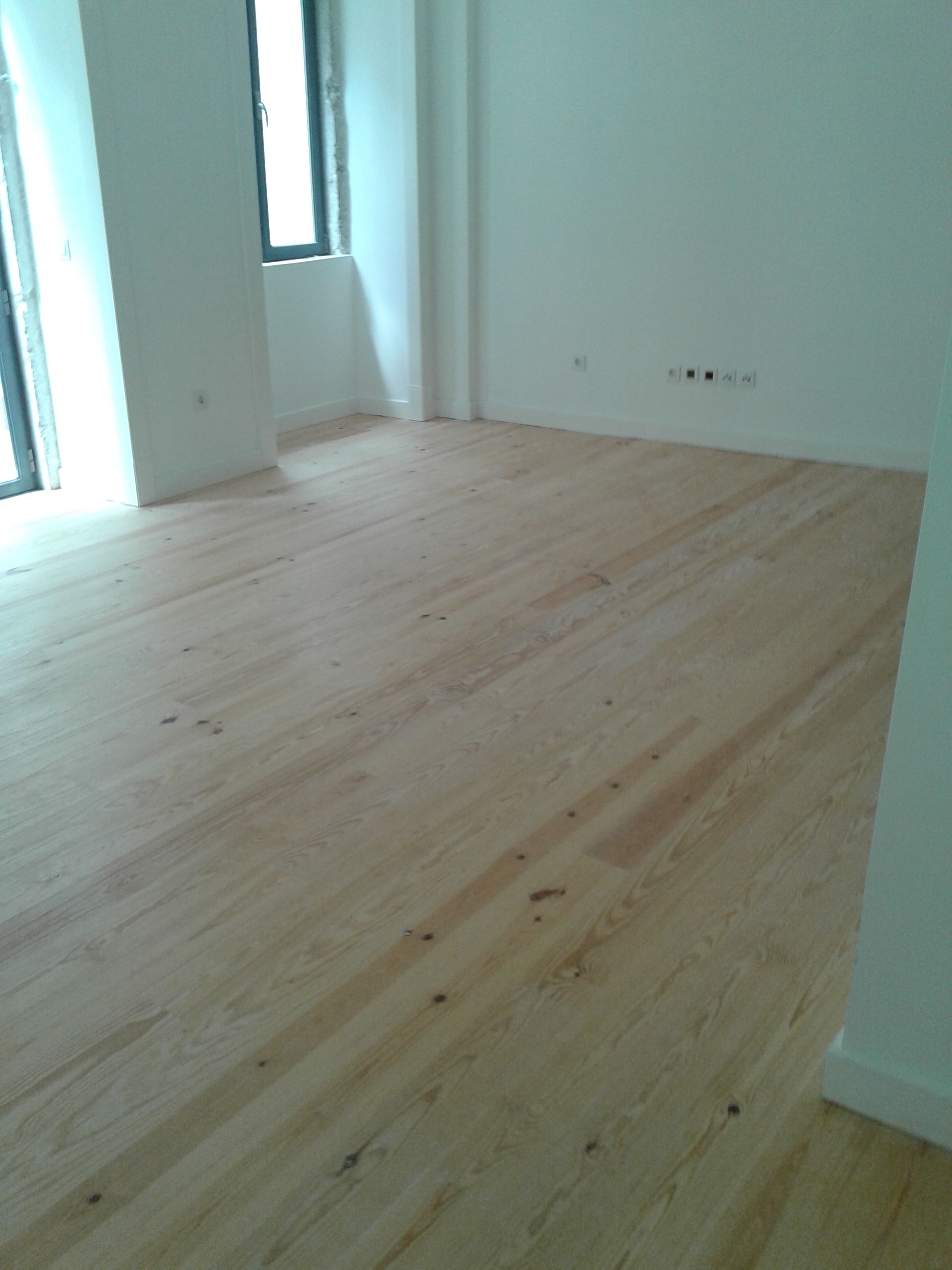 Quarto vazio com piso de madeira clara, paredes brancas e uma janela.