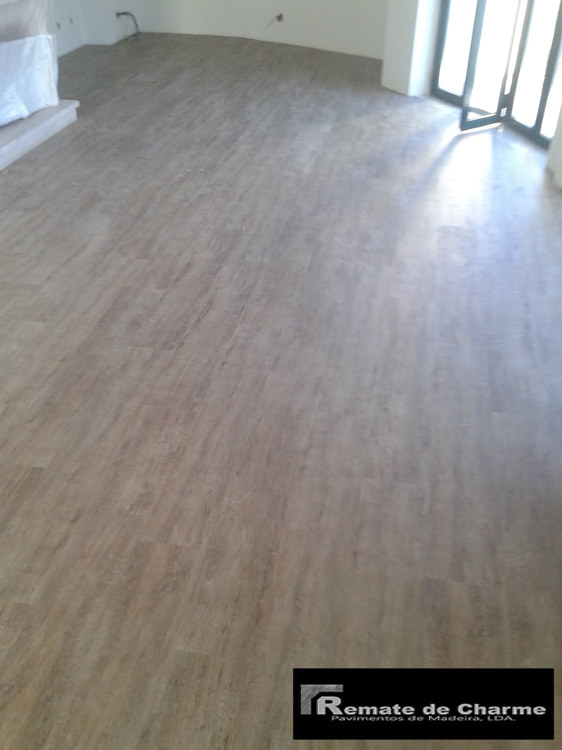 Piso com aparência de madeira clara em uma sala com janela e paredes brancas.