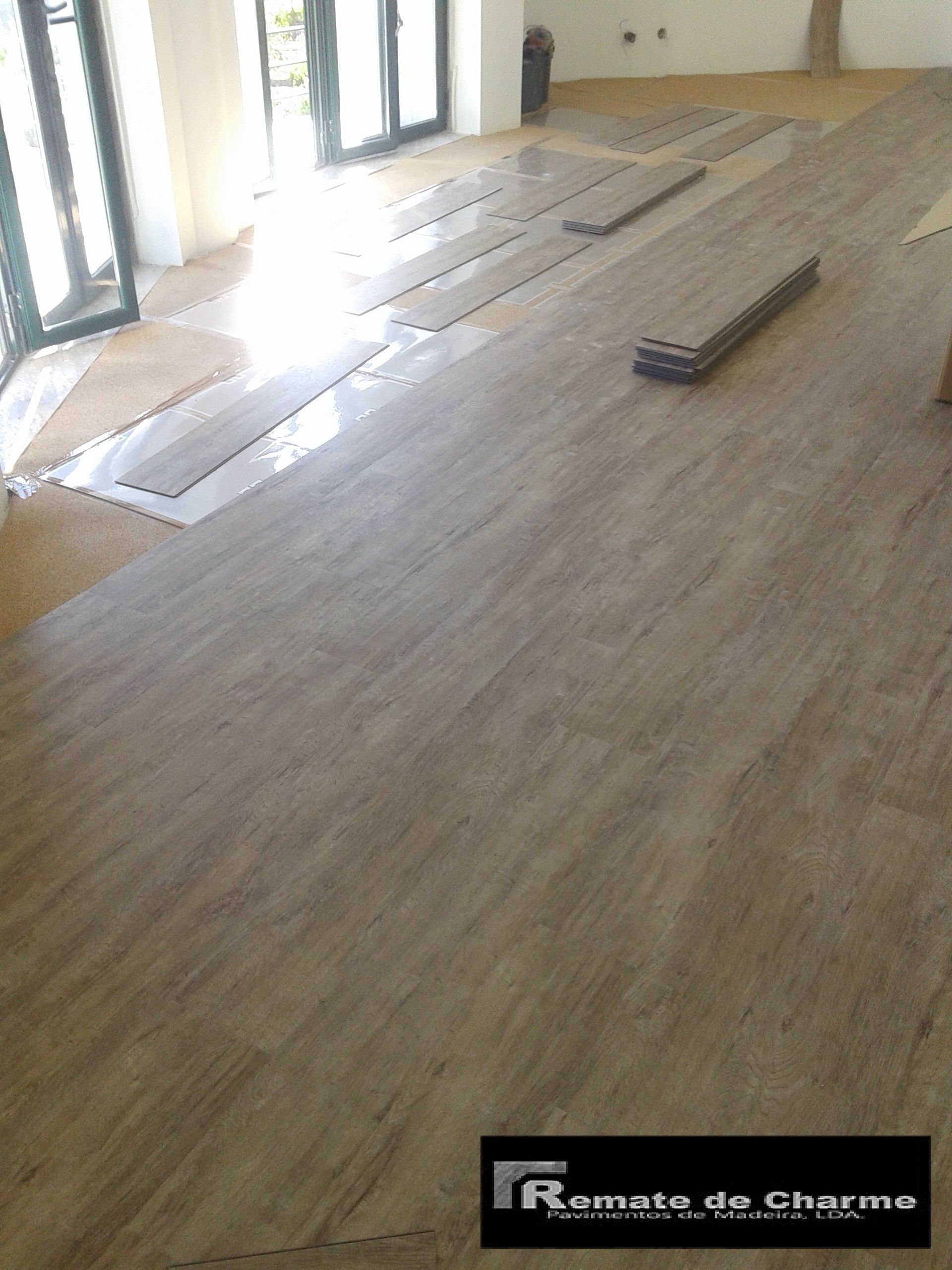Instalação de piso em andamento. Tábuas de madeira dispostas em um cômodo com janelas grandes.