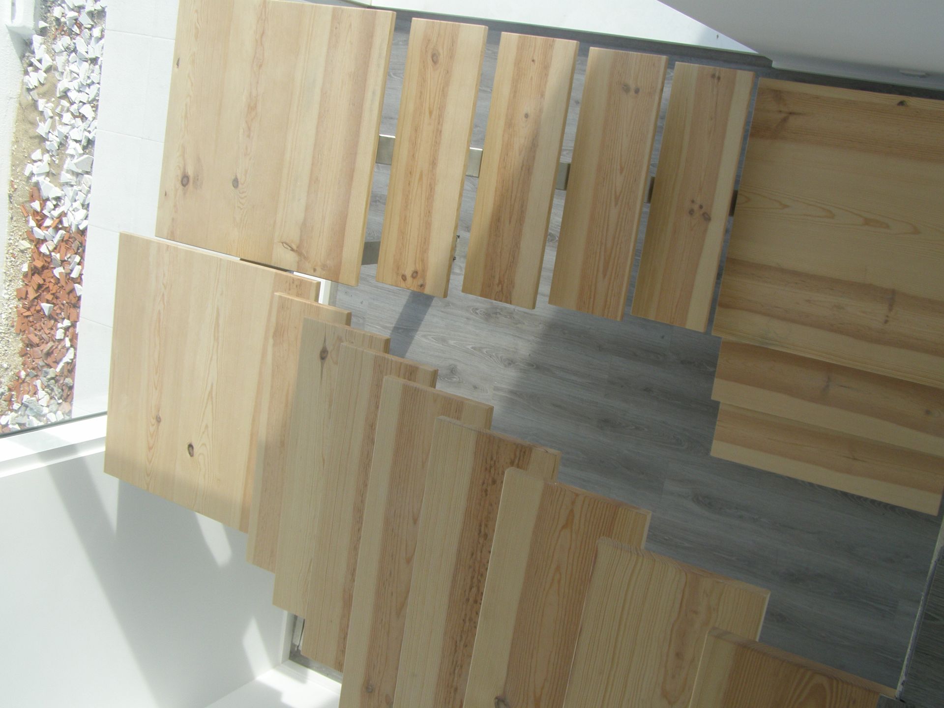 Tábuas de madeira de vários tamanhos e veios, dispostas em leque sobre um piso cinza.