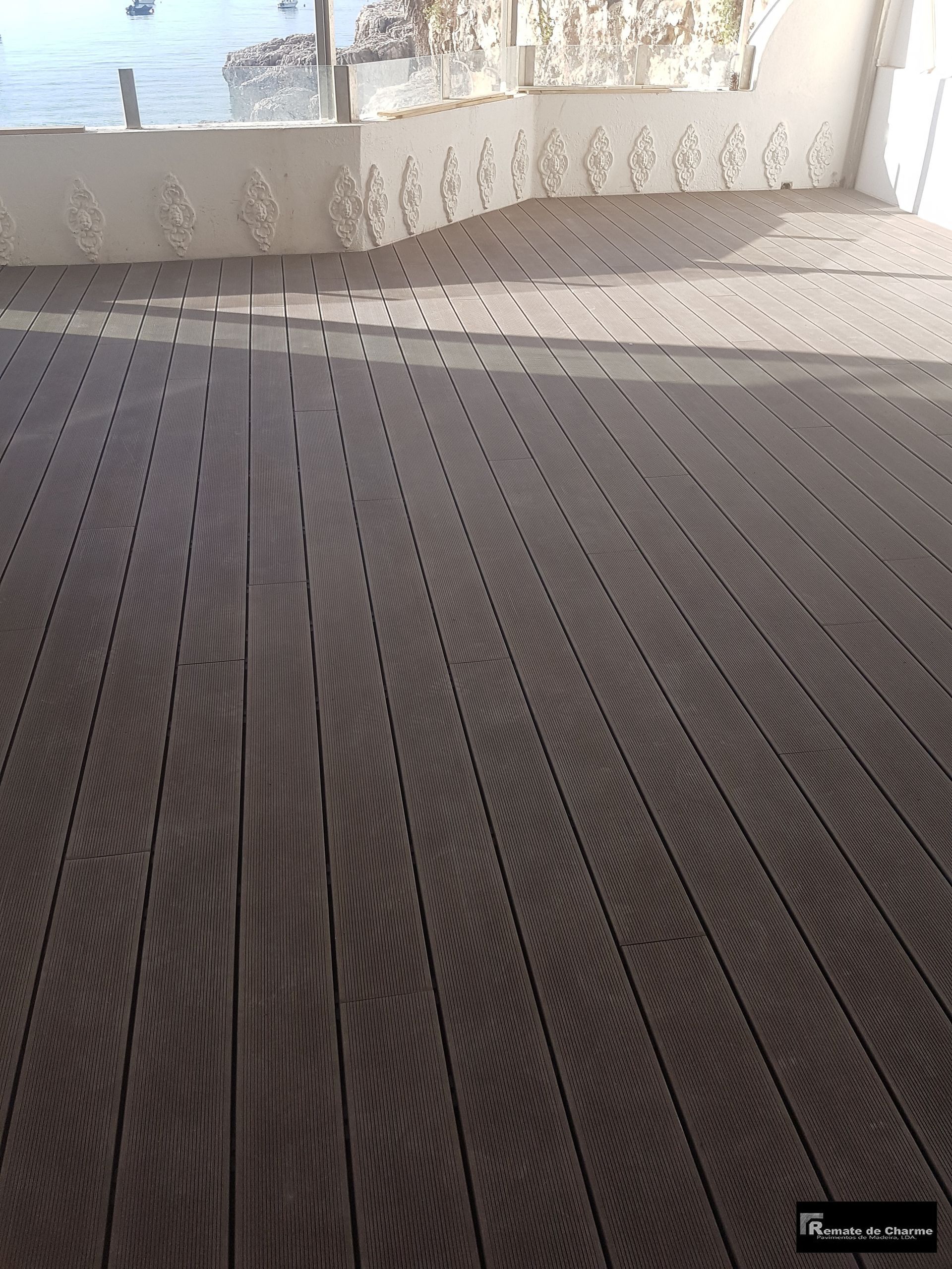 Deck de madeira com corrimão branco ornamentado com vista para um corpo d'água em um dia ensolarado.