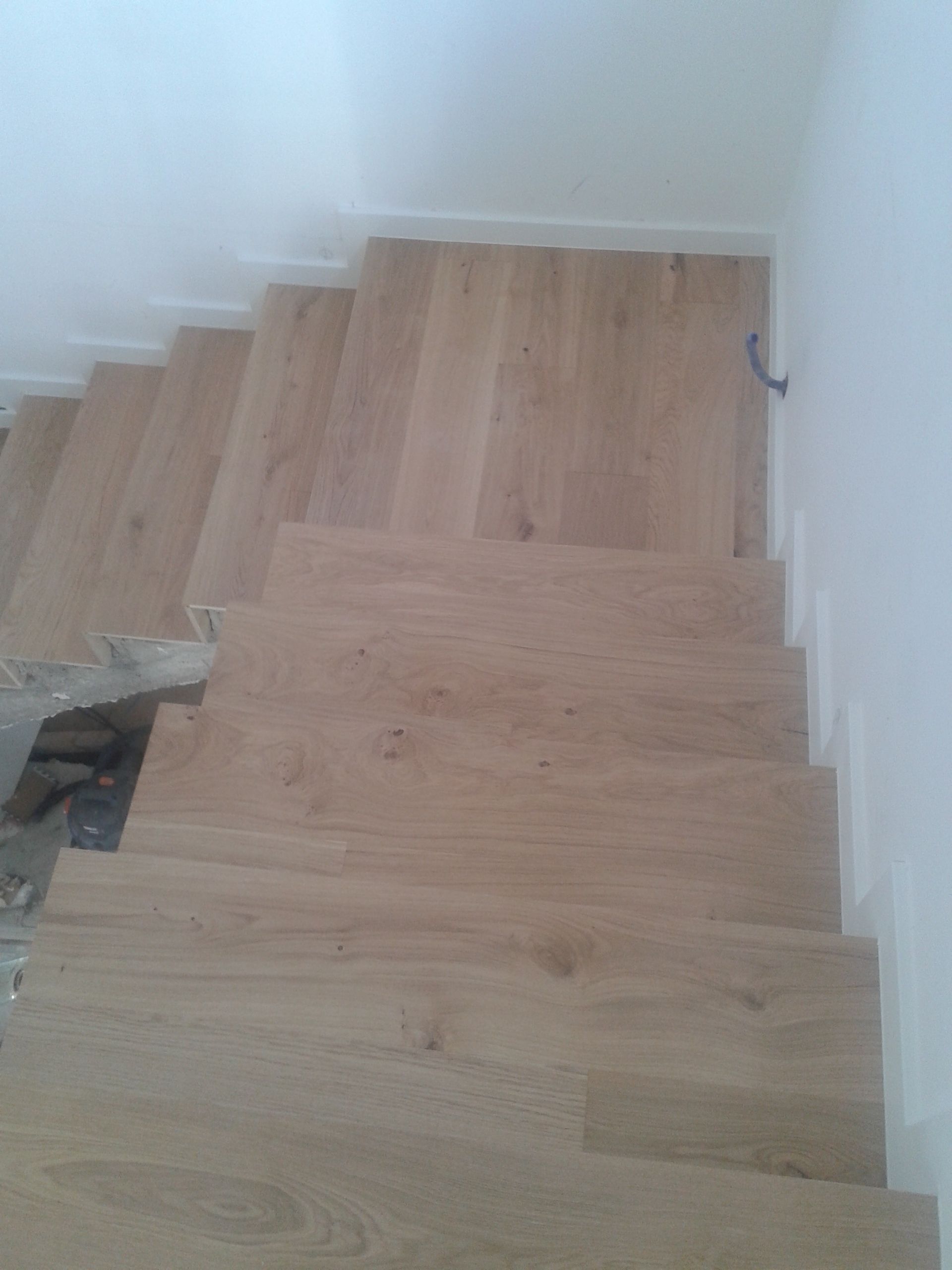 Escada de madeira, degraus de madeira clara, paredes brancas.