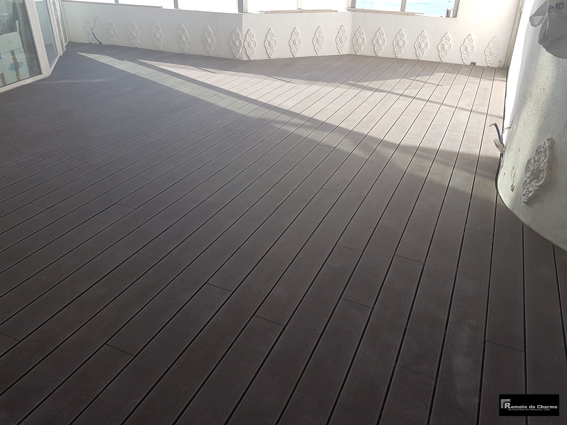 Piso de deck composto cinza em uma varanda, com sombras projetadas pela luz do sol.