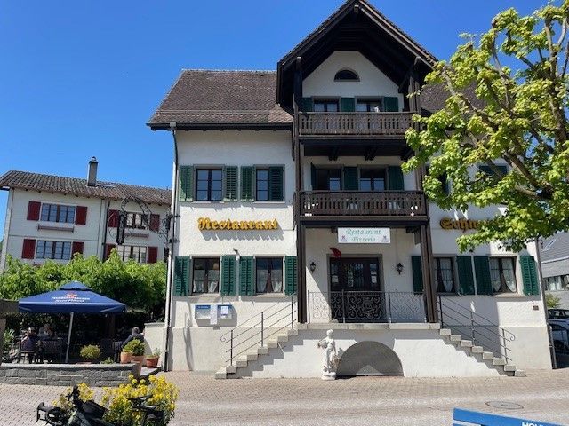 Restaurantgebäude mit Stufen, Balkonen und grünen Fensterläden unter blauem Himmel.