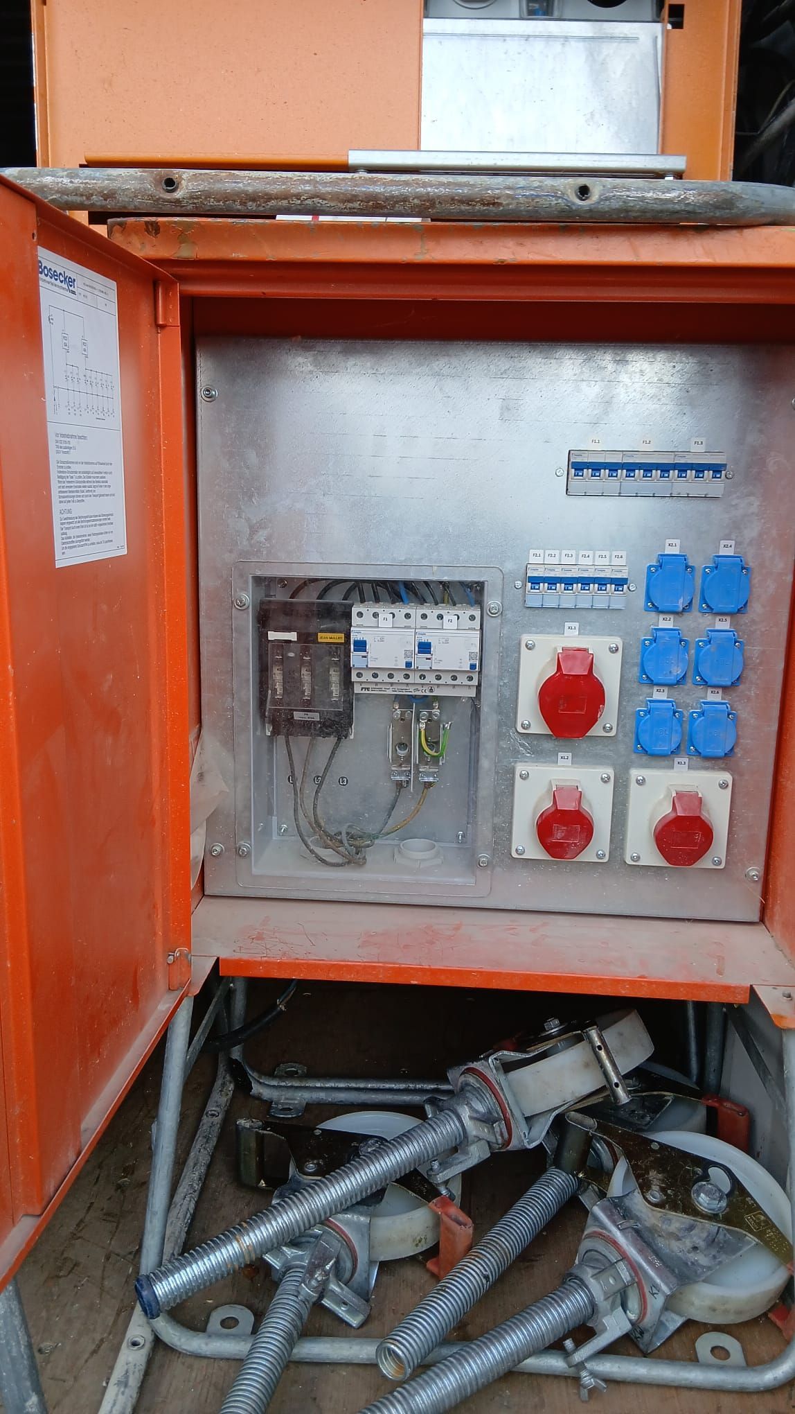 Ein offener, orangefarbener, tragbarer Stromverteilerkasten mit mehreren industriellen Steckdosen und Leistungsschaltern.