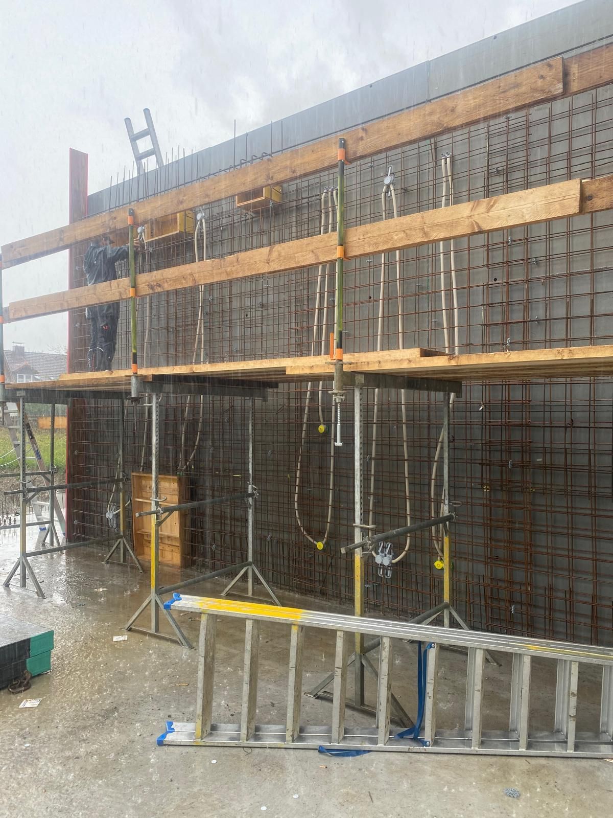 Baustelle mit einer Stahlbetonwand und einer Holzrahmenkonstruktion auf einem Betonboden.