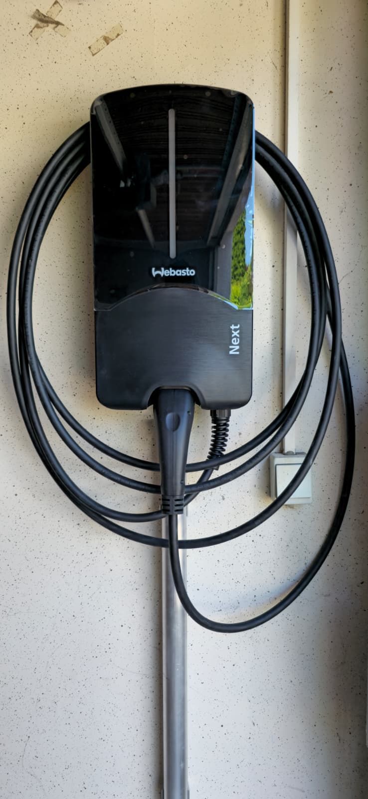 Eine schwarze Wallbox Pulsar Plus Ladestation für Elektrofahrzeuge ist an einer Wand montiert.