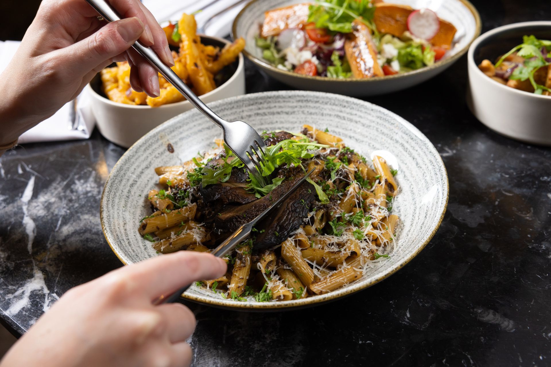 Person eating pasta dish with other food bowls on a table.